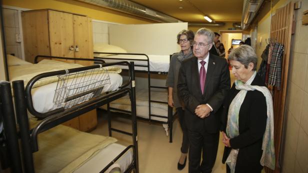 Ein Mann im Anzug und zwei Frauen stehen in einem Raum mit Etagenbetten.