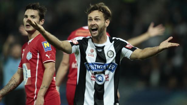 Ein Fußballspieler in einem schwarz-weiß gestreiften Trikot gestikuliert auf dem Spielfeld.