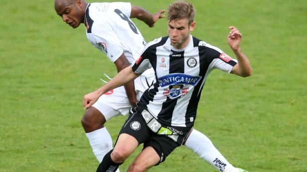 Zwei Fußballspieler kämpfen um den Ball auf dem grünen Rasen.