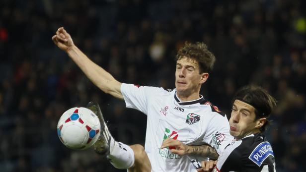 Ein Fußballspieler schießt den Ball, während ein anderer Spieler ihn zu stoppen versucht.