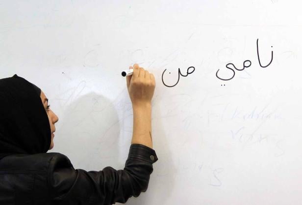 Eine Frau mit Hijab schreibt arabische Schriftzeichen auf eine weiße Tafel.
