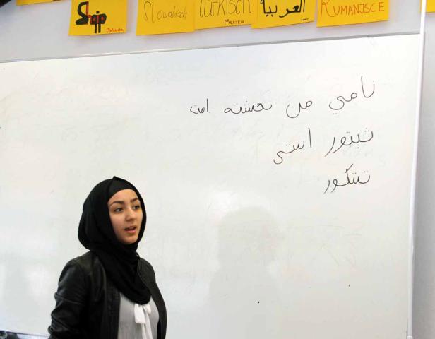 Eine junge Frau steht vor einer Tafel mit arabischer Schrift.