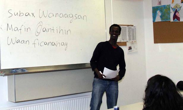 Ein Mann steht vor einer Tafel mit somalischen Wörtern und lächelt.