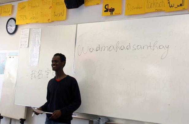 Ein junger Mann steht vor einer Tafel mit verschiedenen Sprachen und Schriftzeichen.