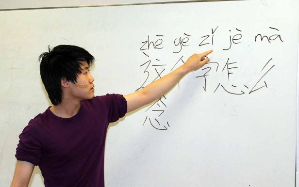 Ein junger Mann erklärt chinesische Schriftzeichen an einer Tafel.