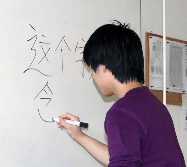 Eine Person schreibt chinesische Schriftzeichen auf eine weiße Tafel.