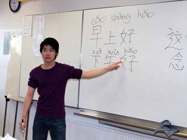 Ein junger Mann erklärt chinesische Schriftzeichen an einer Tafel.