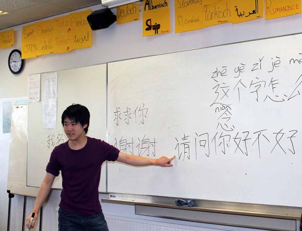 Ein junger Mann erklärt chinesische Schriftzeichen an einer Tafel in einem Klassenzimmer.
