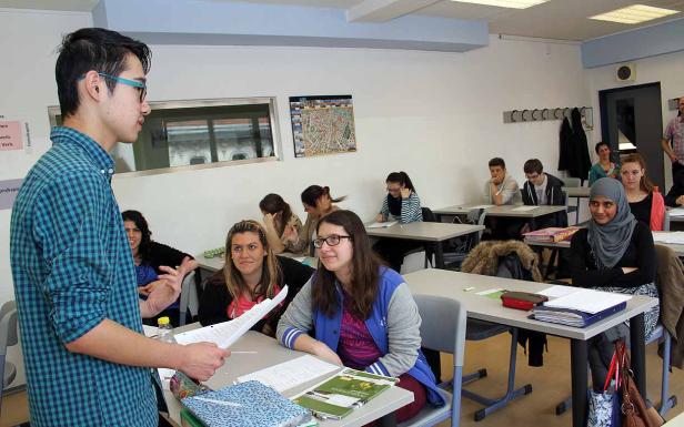 Ein junger Mann präsentiert vor einer Klasse mit Schülern in einem Klassenzimmer.