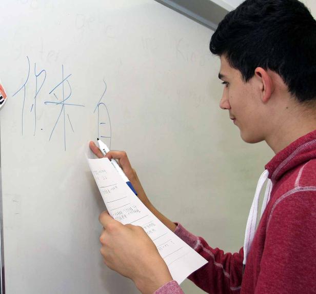 Ein junger Mann schreibt chinesische Schriftzeichen auf eine weiße Tafel.