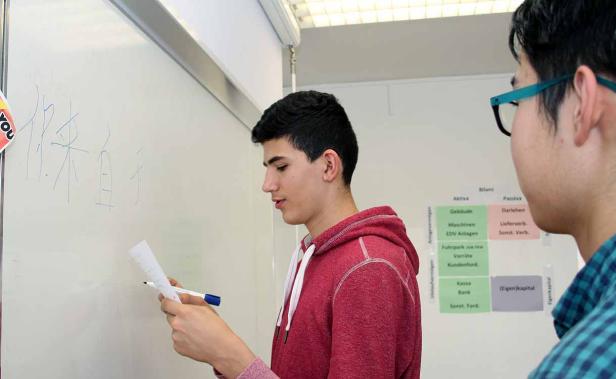 Ein junger Mann schreibt chinesische Schriftzeichen auf eine Tafel.