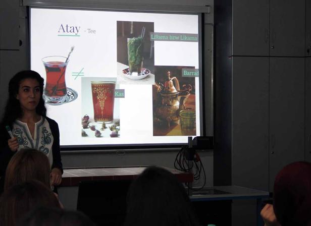 Eine Frau präsentiert eine Folie über Atay-Tee in einem Klassenzimmer.