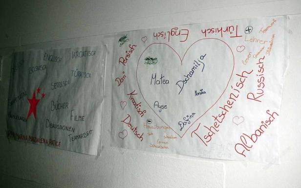 Zwei Poster mit Wörtern und Namen in verschiedenen Sprachen hängen an einer Wand.