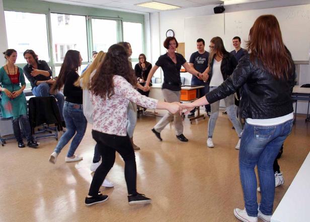 Eine Gruppe von Menschen tanzt im Kreis in einem Klassenzimmer.