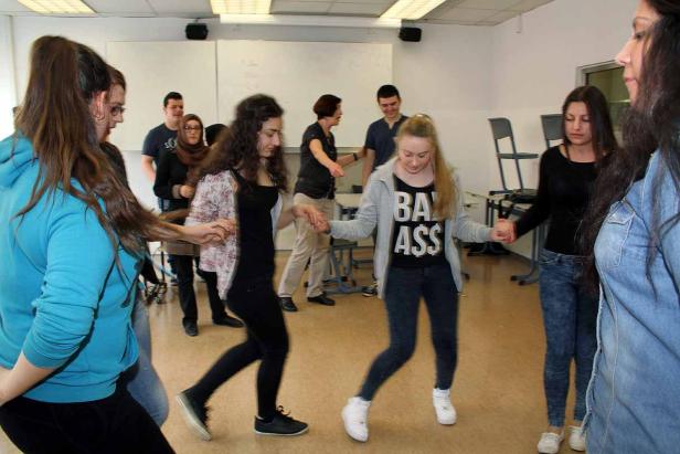 Eine Gruppe junger Leute tanzt im Kreis in einem hellen Raum.