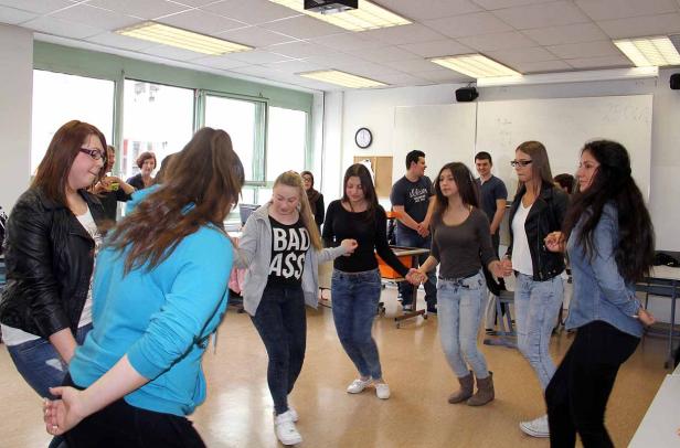 Eine Gruppe junger Leute tanzt im Kreis in einem Klassenzimmer.