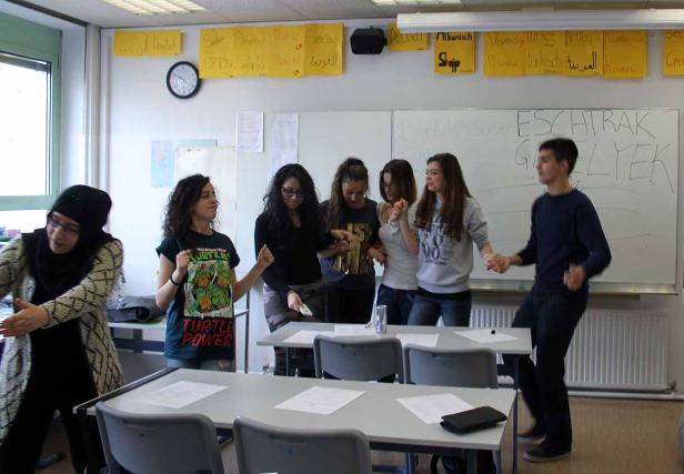 Eine Gruppe von Schülern tanzt in einem Klassenzimmer vor einer Tafel.