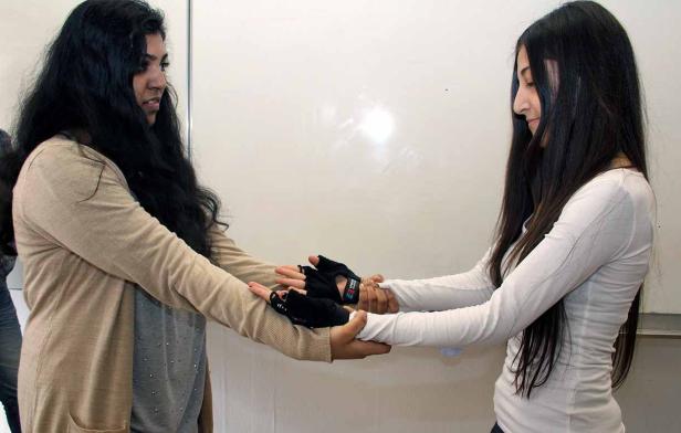 Zwei Frauen halten sich an den Händen, wobei eine Handschuhe trägt.