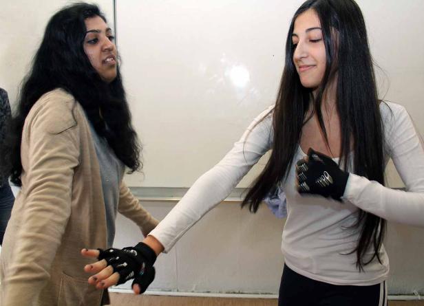 Zwei junge Frauen tragen Handschuhe mit Sensoren und scheinen miteinander zu interagieren.