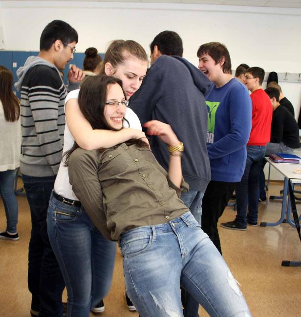 Eine Gruppe von Teenagern umarmt sich und lacht in einem Klassenzimmer.