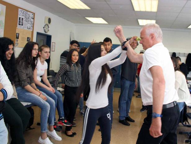 Eine junge Frau übt Selbstverteidigung mit einem älteren Mann vor einer Gruppe von Zuschauern.