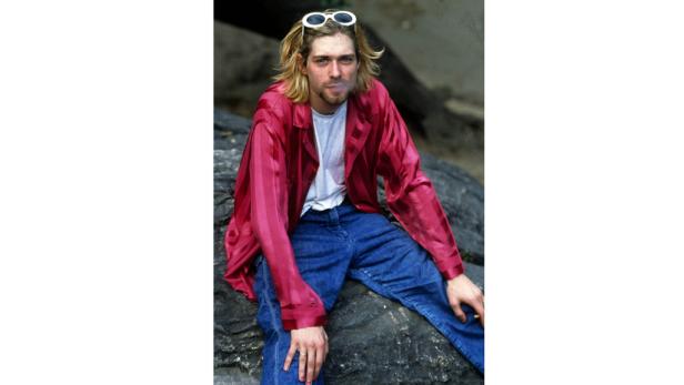 Kurt Cobain sitzt mit einer Zigarette auf einem Felsen.