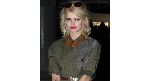 Eine Frau mit blonden Haaren, rotem Lippenstift und einer auffälligen Kette.