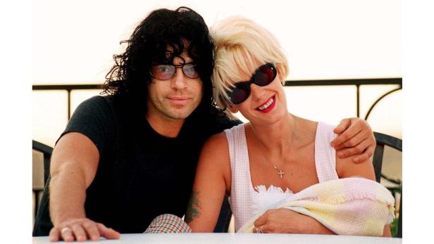 Ein Mann mit dunklen Locken und Brille posiert mit einer blonden Frau mit Sonnenbrille.