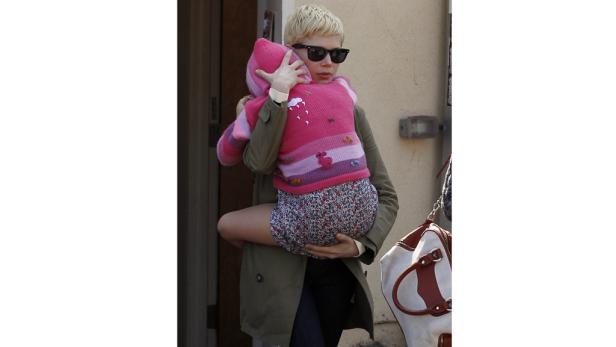 Michelle Williams trägt ein Kind mit einem rosa Pullover mit Tiermotiven.