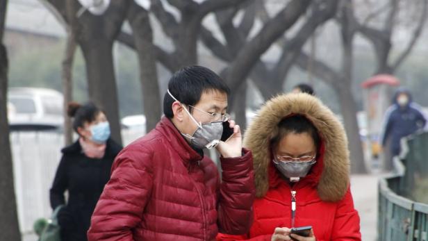 Menschen mit Gesichtsmasken gehen auf einer Straße entlang und benutzen ihre Smartphones.