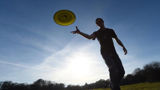 Ein Mann wirft eine gelbe Frisbee vor blauem Himmel.