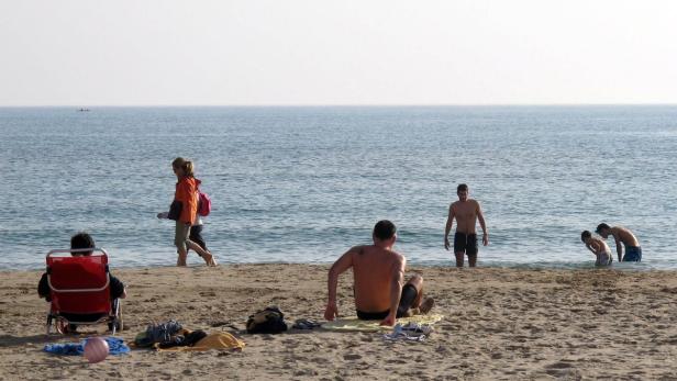 Menschen entspannen sich an einem sonnigen Strand am Meer.