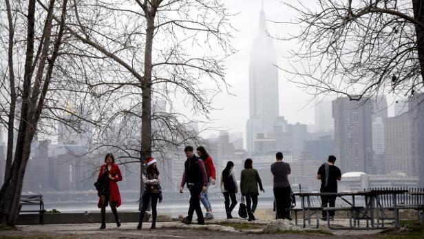 Eine Gruppe von Menschen spaziert vor der Skyline von New York City an einem trüben Tag.