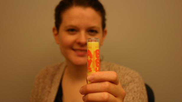 Eine Frau hält einen gelben „Baby Lips“-Lippenpflegestift in die Kamera.