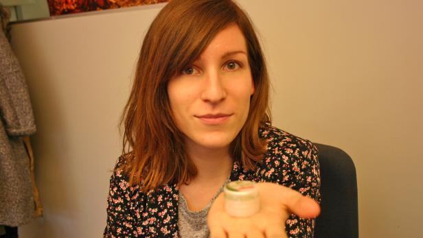 Eine Frau präsentiert ein kleines Döschen mit Creme in ihrer Hand.