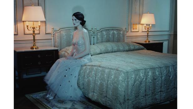 Eine Frau im Abendkleid sitzt auf einem Bett in einem eleganten Zimmer.