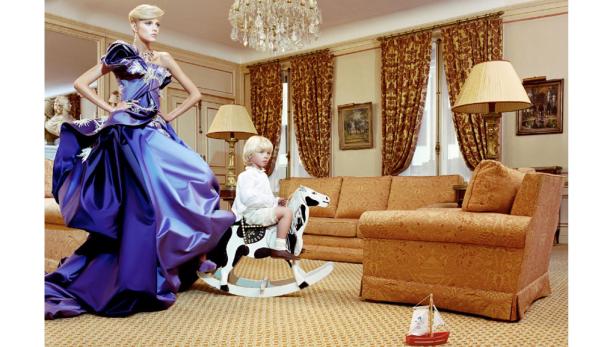 Eine Frau im Abendkleid steht neben einem Jungen, der auf einem Schaukelpferd reitet.