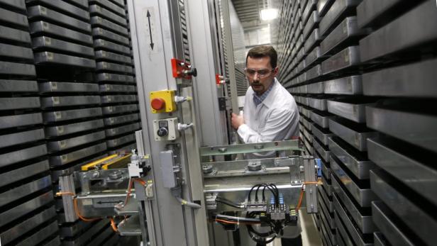 Ein Mann in Laborkittel und Schutzbrille bedient eine automatisierte Lageranlage.