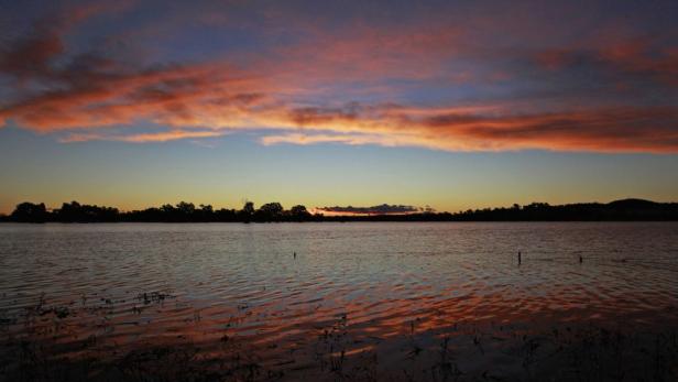 Ein ruhiger See spiegelt den orangefarbenen Himmel bei Sonnenuntergang wider.