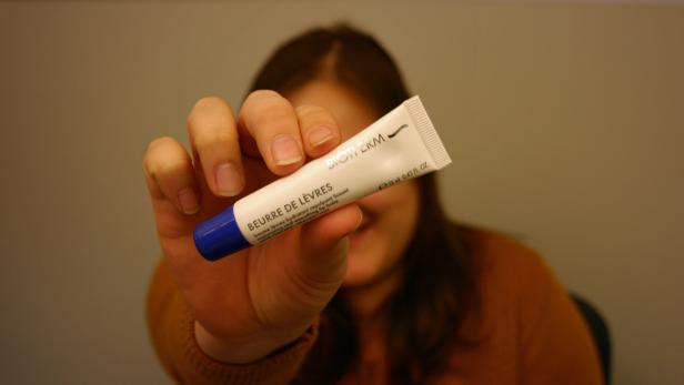 Eine Frau hält einen Lippenpflegestift von Biotherm in der Hand.