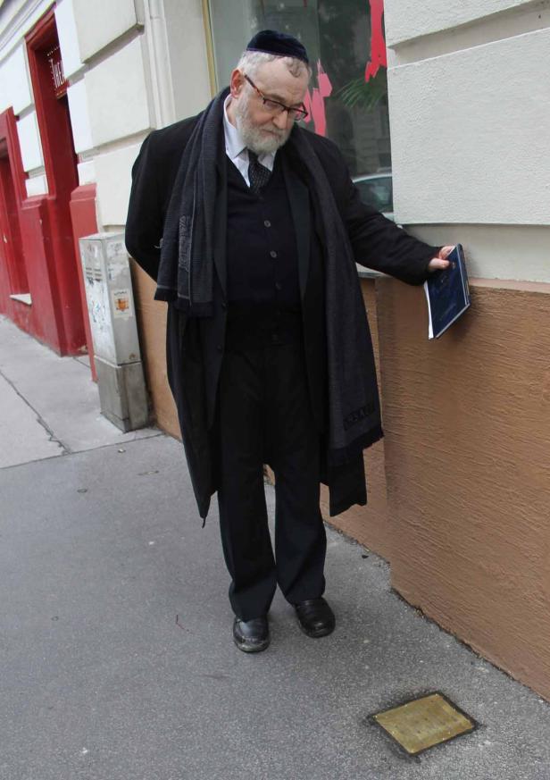 Ein Mann mit Kippa betrachtet einen Stolperstein vor einem Gebäude.