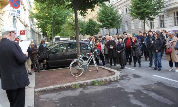 Eine Gruppe von Menschen steht auf einer Straße und hört einem Redner zu.