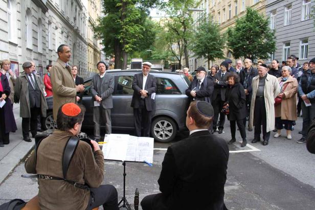 Eine Gruppe von Menschen versammelt sich auf einer Straße, während ein Mann spricht und ein Musiker spielt.