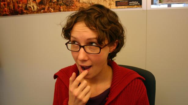 Eine Frau mit Brille und rotem Pullover berührt ihre Lippe mit dem Finger.