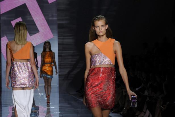 Eine Frau auf dem Laufsteg präsentiert ein orangefarbenes und rotes Paillettenkleid.