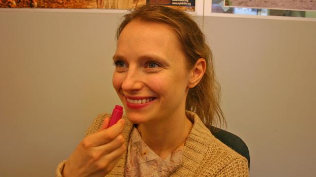 Eine Frau lächelt und hält einen pinkfarbenen Lippenpflegestift in der Hand.