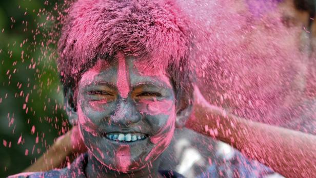 Ein Junge ist mit rosa Farbe während des Holi-Festivals bedeckt.
