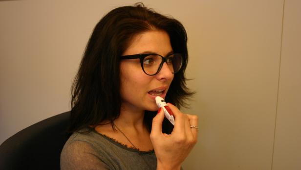 Eine Frau mit Brille trägt Lippenbalsam auf.