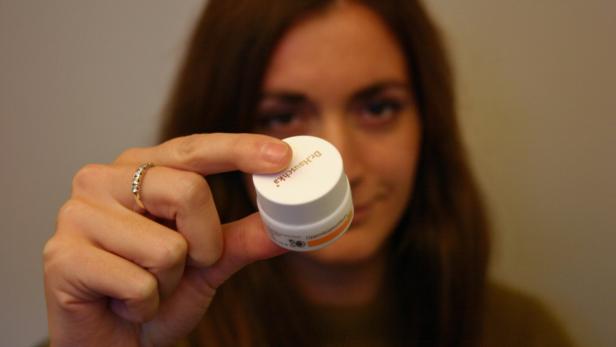 Eine Frau hält eine Dose Dr. Hauschka Lippenkosmetik in der Hand.