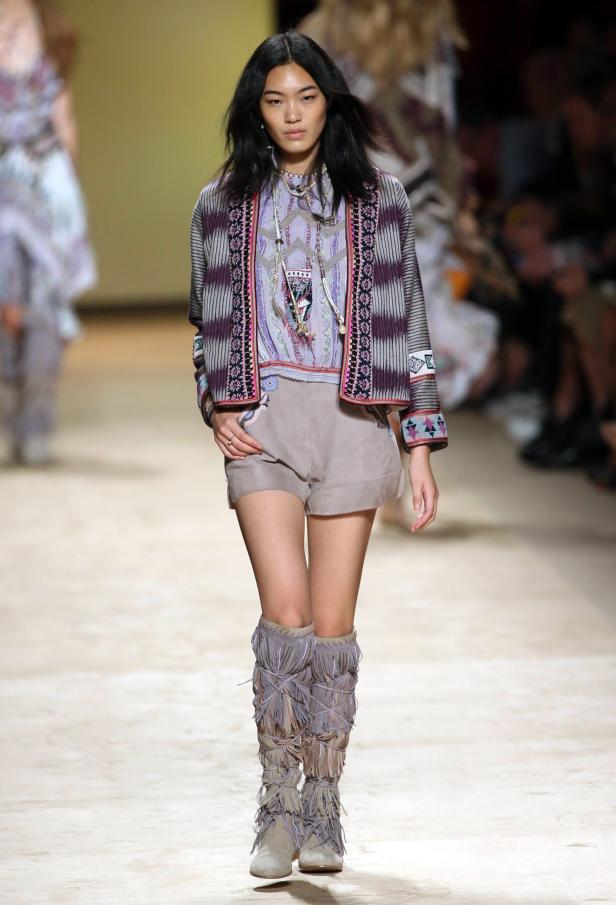 Eine Frau präsentiert ein Outfit mit Shorts und Fransenstiefeln auf dem Laufsteg.